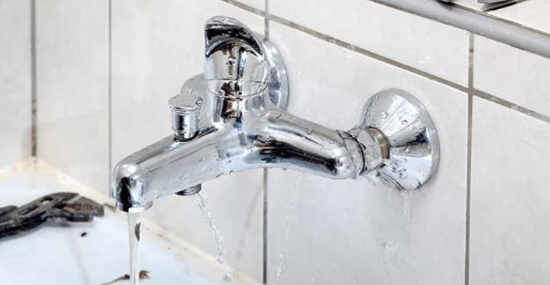 Water leaking from a chrome wall-mounted faucet